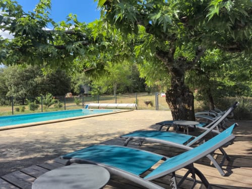 Sunny poolside lounge at Domaine en Terre Happy, Labastide-de-Virac, with blue deck chairs under a large tree