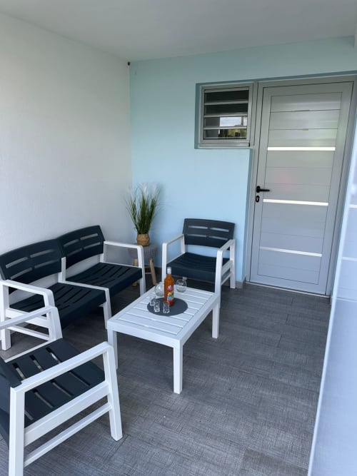 Élégant coin détente sur la terrasse de Maly Blue Location au Moule avec mobilier blanc, coussins noirs et accès par porte vitrée