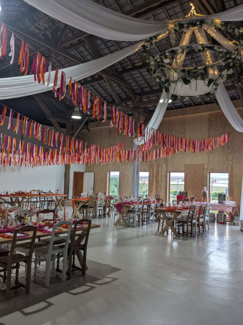 Salle de banquet élégante du Domaine De La Souche avec guirlandes de rubans rouges, draperies blanches et lustre décoré pour événements.