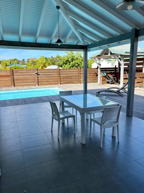 Élégante terrasse piscine à Maly Blue Location au Moule avec table de repas, chaises longues et clôture en bois sous ciel bleu