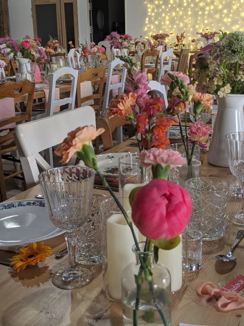 Élégante salle de banquet du Domaine De La Souche avec arrangements floraux roses et corail, chaises en bois et guirlandes lumineuses chaleureuses