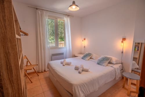 Chambre lumineuse à la villa Residence Guddelmoni à Propriano avec literie blanche, mobilier en bois, vue sur jardin et ambiance chaleureuse