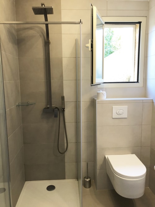 Salle de bains moderne de la villa de Propriano avec douche à l'italienne, toilettes et fenêtre avec vue sur le jardin