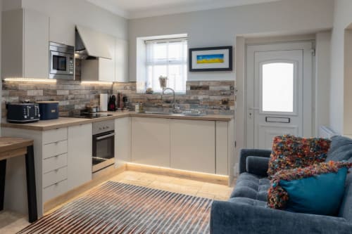 Modern kitchen and living area at The Ford Apartment in Perth, featuring cream cabinetry, brick backsplash, and comfortable