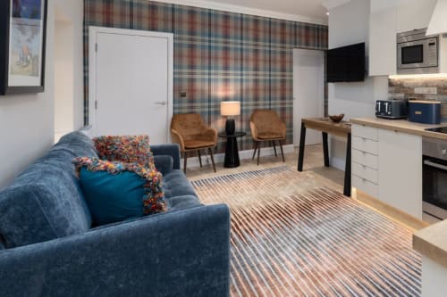 The Ford Apartment in Perth: modern studio with blue sofa, tan armchairs, plaid accent wall, kitchen, and striped rug