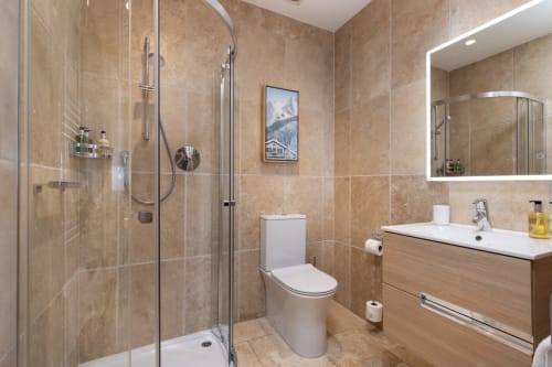 Modern bathroom at The Ford Apartment Perth with walk-in shower, white toilet, wooden vanity, and illuminated mirror