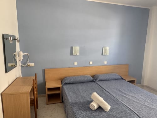 Habitación moderna en Apartamentos Playa Sol con cama de madera, ropa de cama gris, escritorio y pared azul en Es Canar