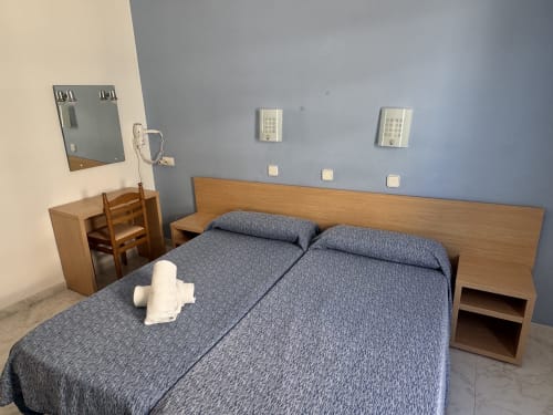 Habitación moderna del hotel Apartamentos Playa Sol con cama doble, muebles de madera y paredes azules en Es Canar