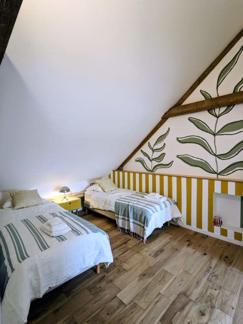 Chambre cosy sous les toits à la Domaine De La Souche avec deux lits, tête de lit aux rayures jaunes, poutres en bois et décoration botanique