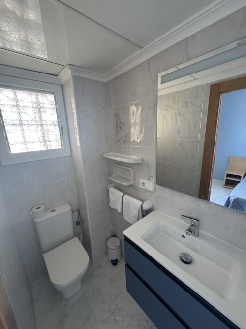 Baño moderno en Apartamentos Playa Sol, Es Canar, con azulejos blancos, mueble azul, inodoro, lavabo y ducha