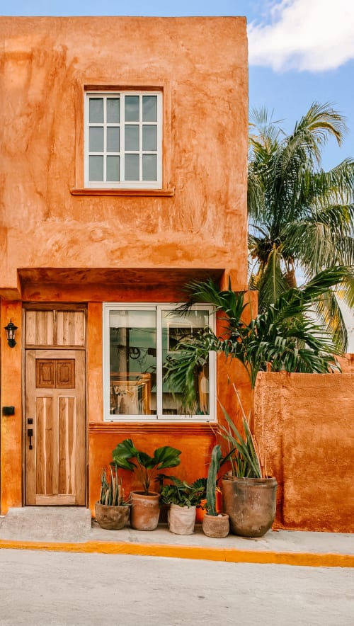 Vibrant orange cottage in Isla Mujeres with wooden door, window, and potted tropical plants on street