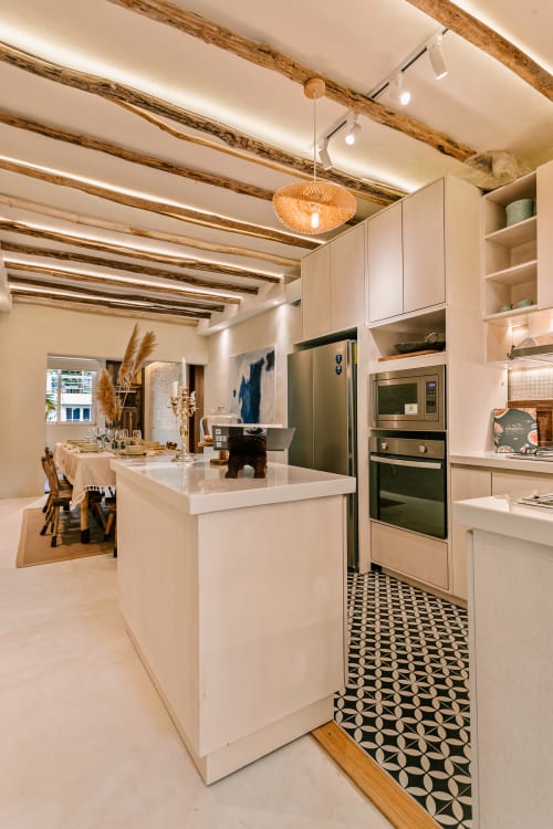 Modern cottage kitchen with white island, green appliances, exposed wooden beams, pendant lighting, and geometric tile