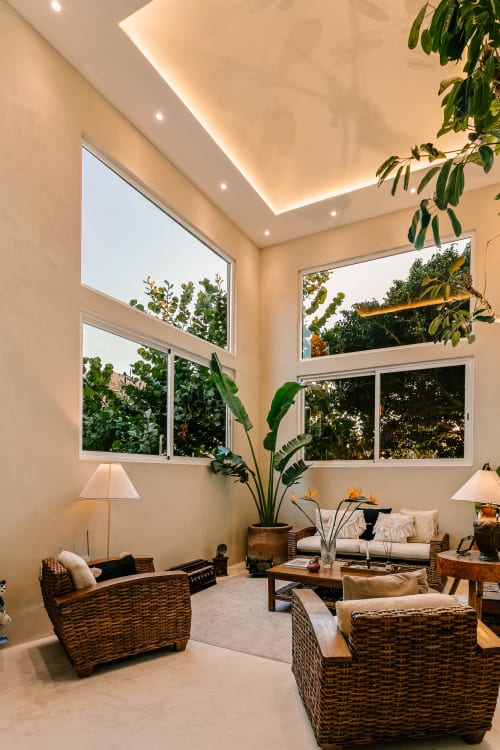 Modern living room at Casa Rocka Isla Mujeres with woven furniture, plants, and large windows overlooking tropical garden