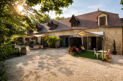 Cour du Domaine de Valenquercy avec bâtisses en pierre, zones ombragées et jardins verdoyants à Le Vignon-en-Quercy