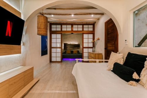 Modern cottage bedroom at Casa Rocka in Isla Mujeres with wooden beams, arched ceiling, flat-screen TV, and access to living
