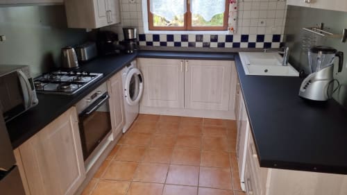 Cuisine avec placards crème, plan de travail noir, cuisinière à gaz et carrelage terre cuite à Le Clos du Tay, La Gacilly