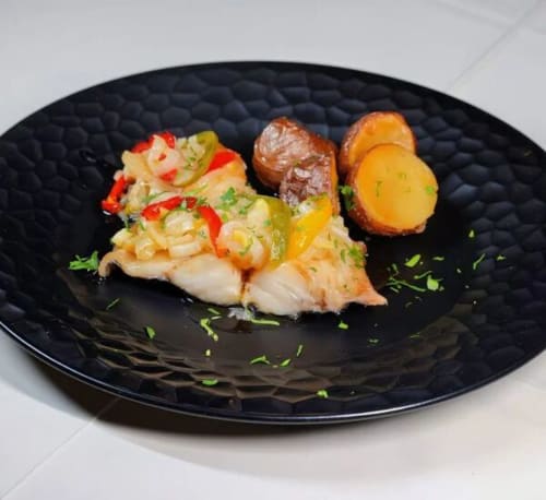 Prato gourmet de frutos do mar apresentado na Tranca da Barriga Casa do Vinho em Covilhã, com peixe assado, vegetais e ervas sobre fundo preto