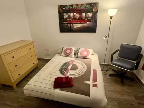 Mira Barna apartment bedroom with white bed, pink accessories, wooden dresser, and Pershing Square artwork in Barcelona