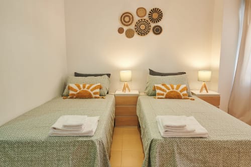 Twin bedroom with green patterned bedspreads, orange sunrise pillows, and woven basket wall décor at Mediterranea Sunny Keys,
