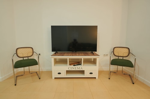 Sunny apartment living room with TV, white entertainment unit labeled CINEMA, and two vintage-style chairs at Mediterranea