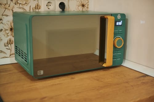 Vintage green microwave with wooden handle on wooden surface in Mediterranea Sunny Keys apartment, Castelló de la Plana