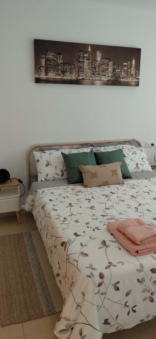 Chambre lumineuse à Mediterranea Sunny Keys avec literie florale, oreillers verts et toile de la skyline de New York