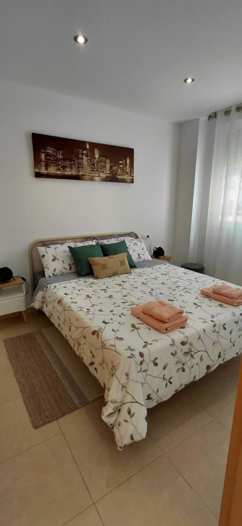 Chambre lumineuse à Mediterranea Sunny Keys avec literie florale, tableau panoramique urbain, éclairage encastré moderne et murs blancs