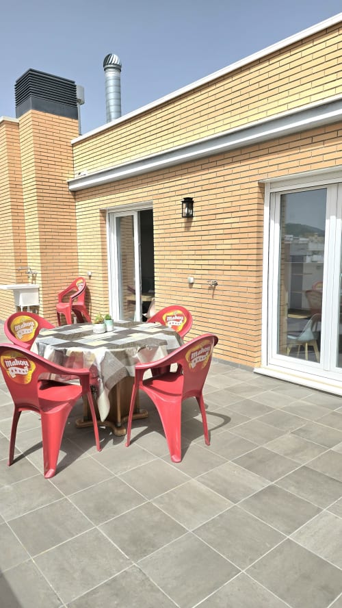 Sunny terrace at Mediterranea Sunny Keys in Benicàssim with red chairs and table, brick building, clear sky