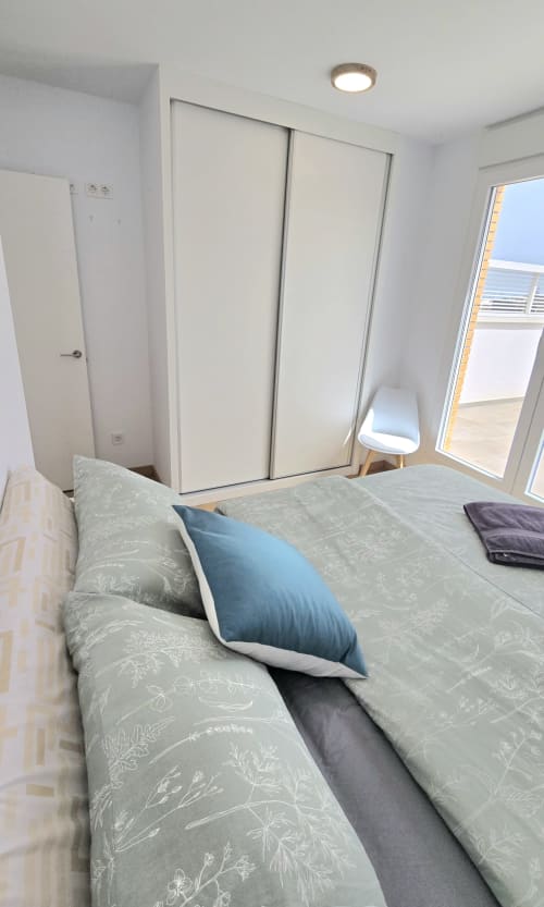Modern bedroom in Benicàssim apartment with queen bed, blue pillow, sliding wardrobe, and sliding doors to balcony