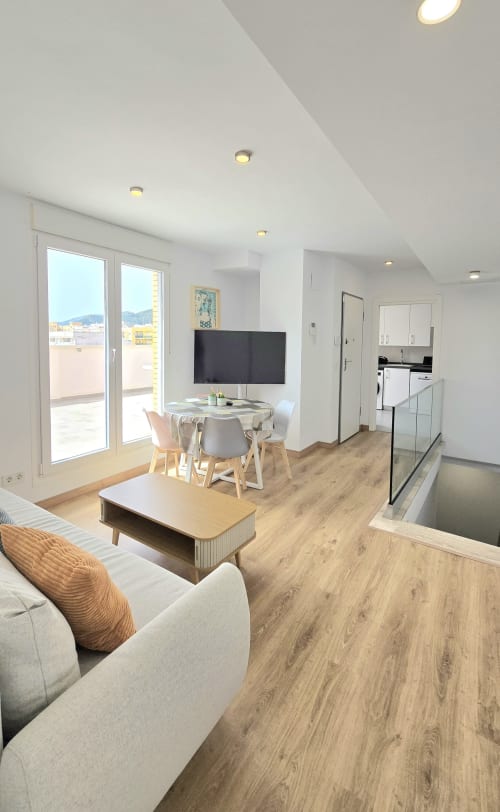 Moderno salón con comedor, televisión de pantalla plana, suelo de madera y balcón con vistas a las montañas en Benicàssim