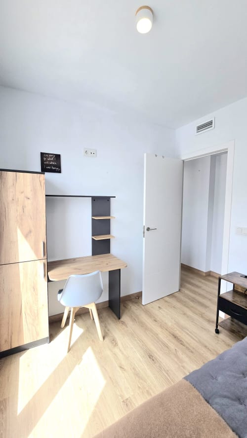 Modern studio apartment in Benicàssim with wooden desk, white chair, kitchenette, and bright natural light from ceiling