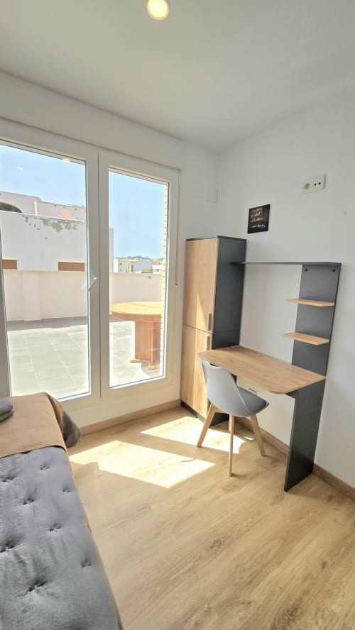 Modern studio apartment in Benicàssim with wooden desk, chair, shelving, and terrace access with mountain views