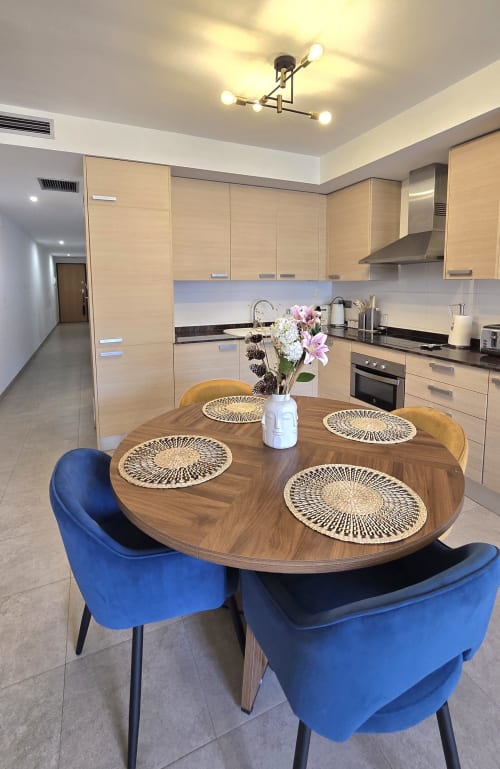 Cocina-comedor moderno con mesa redonda de madera, sillas de terciopelo azul y muebles de madera clara, Els Dolors Sunny Flat