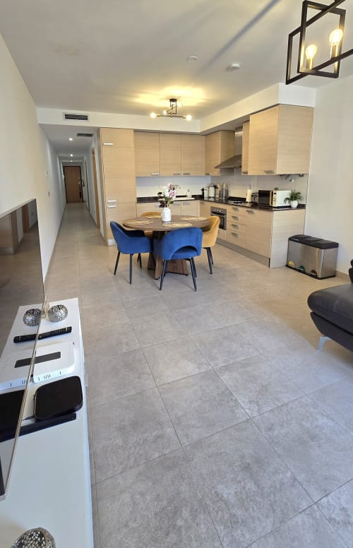 Modern kitchen-dining area in Els Dolors Sunny Flat, Benicàssim apartment with light wood cabinets, blue chairs, and tile