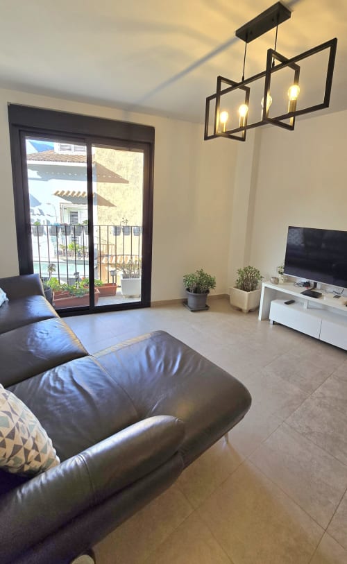 Modern living room with leather sofa, flat-screen TV, black geometric pendant lights, and glass balcony doors overlooking
