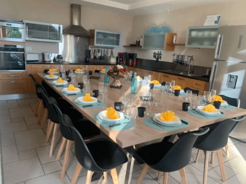 Élégante salle à manger du gîte L'etoile Filante avec table en bois massif, chaises noires, couverts aux serviettes jaunes