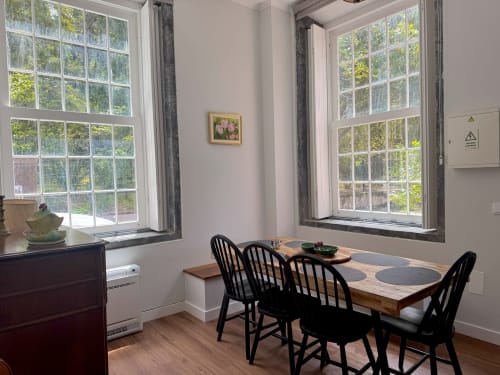 Bright dining area in Casa Dos Barcos cottage with wooden table, black chairs, and large windows overlooking Furnas lake