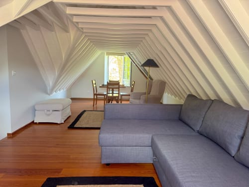 Bright attic cottage bedroom in Furnas with gray sofa, wooden floors, sloped ceilings, desk by window with lake view