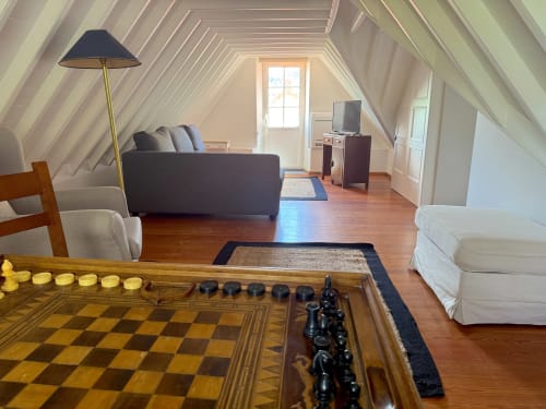 Bright attic room in Furnas cottage with chess set, sofa, TV, white armchairs, and wooden flooring