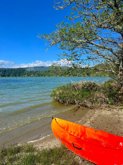 Bright red kayak on sandy beach by Furnas lake, São Miguel, with forested mountains and blue sky