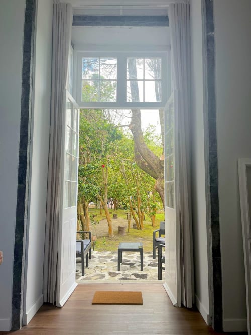 Open French doors framing tree-lined garden courtyard with seating area at Casa Dos Barcos, Furnas cottage