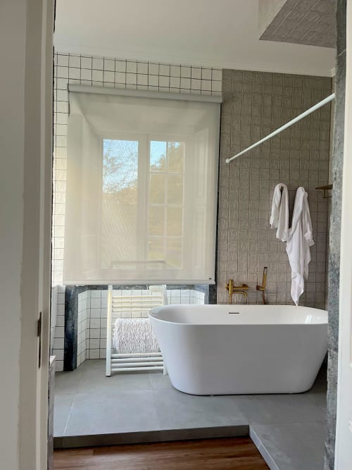 Modern white freestanding bathtub in spa-like bathroom with gray tiling, towel rack, and window view at Casa Dos Barcos