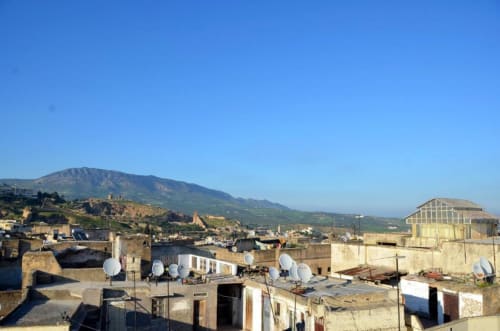 Vue de la médina de Fès depuis la terrasse du Riad Dar Tahri : architecture traditionnelle, antennes satellites et montagnes de l'Atlas en arrière-plan