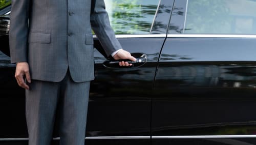 Homme d'affaires en costume gris déverrouillant sa voiture de luxe devant le Riad Dar Tahri à Fès