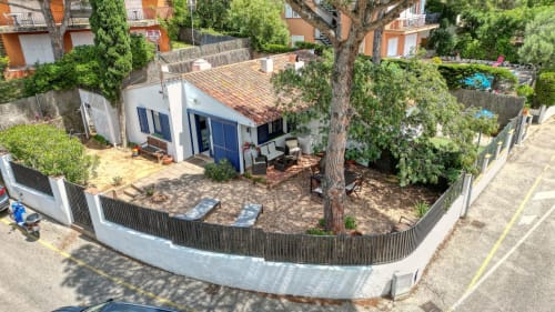 Caseta blanca amb portes blaves, jardí privat amb arbres grans, tancament de fusta i zona de descans exterior a Palafrugell, Espanya