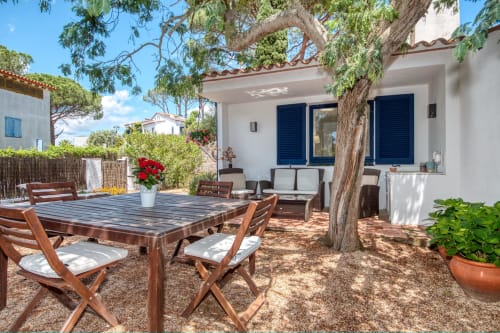 Pati de jardí privat amb taula de menjador de fusta, cadires i gran arbre de la casa rural Casa Golfet a Palafrugell