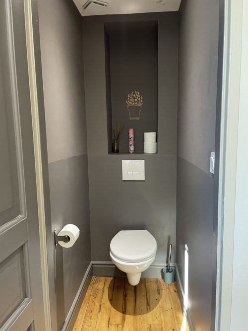 Modern bathroom with white toilet, gray walls, wooden floor, and decorative shelf with cactus art at Maunoury Citybreak