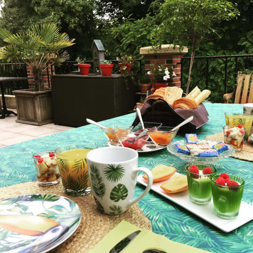 Outdoor rooftop brunch setup at Maunoury Citybreak in Chartres with tropical-themed table, pastries, beverages and garden