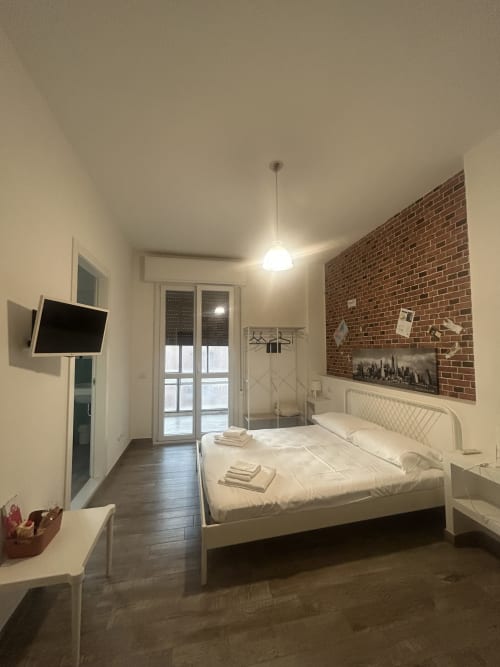 Camera moderna del B&B Gate 10 Fiera Bologna con letto bianco, parete in mattoni, TV a schermo piatto e doccia in vetro a Bologna