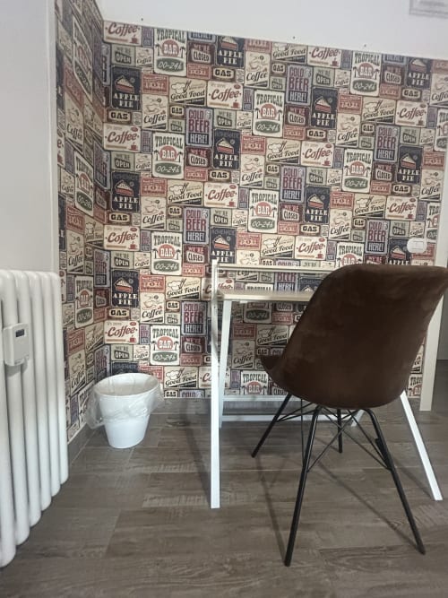 Angolo moderno con carta da parati vintage stile caffetteria e diner, sedia marrone e cestino bianco presso B&B Gate 10 Bologna